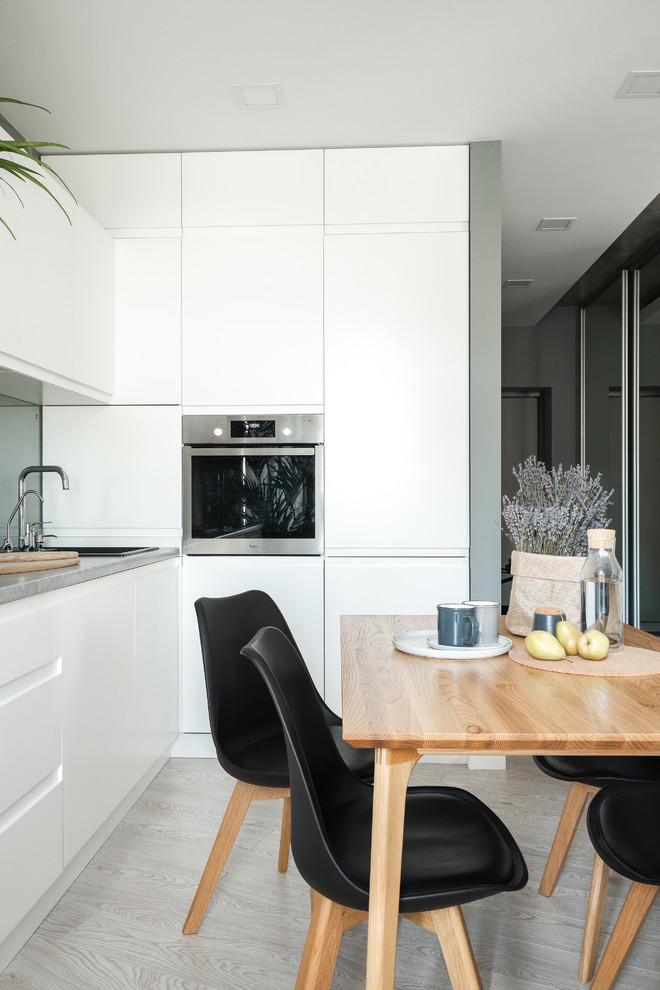 Design ideas for a scandinavian l-shaped open plan kitchen in Other with a drop-in sink, flat-panel cabinets, stainless steel appliances, light hardwood floors, grey floor, grey benchtop, mirror splashback and no island.