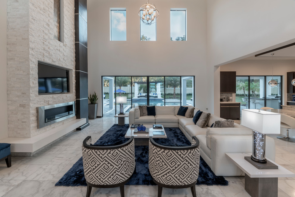Design ideas for an expansive contemporary open concept family room in Orlando with white walls, marble floors, a stone fireplace surround, a wall-mounted tv and white floor.