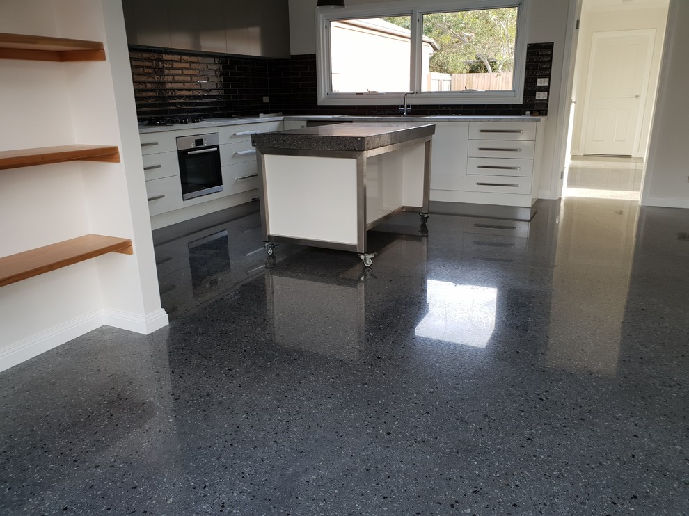 Mid-sized contemporary open plan kitchen in Melbourne with white cabinets, concrete benchtops, black splashback, ceramic splashback, stainless steel appliances, concrete floors, with island, black floor and black benchtop.