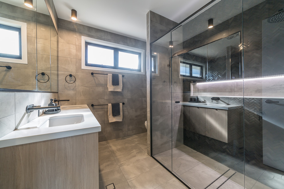 Photo of a mid-sized contemporary 3/4 bathroom in Brisbane with light wood cabinets, a freestanding tub, a corner shower, a two-piece toilet, gray tile, ceramic tile, grey walls, ceramic floors, an undermount sink, engineered quartz benchtops, grey floor, a hinged shower door and white benchtops.