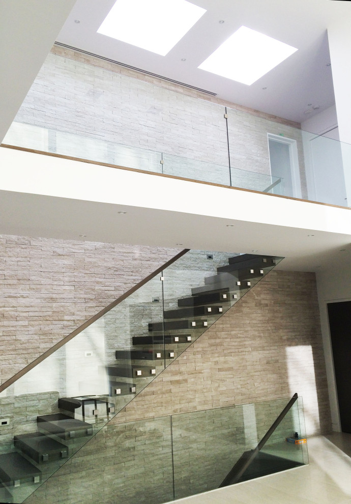 トロントにあるモダンスタイルのおしゃれな直階段 (ガラスの蹴込み板、木材の手すり、レンガ壁) の写真