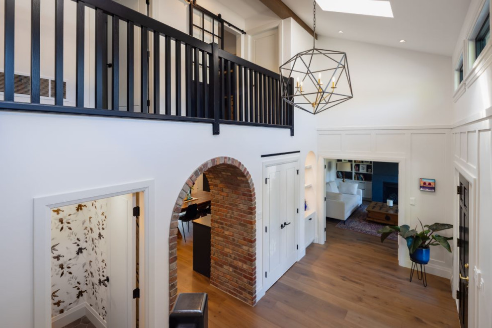 Mid-sized transitional medium tone wood floor, brown floor and wall paneling foyer photo in Vancouver with white walls and a black front door