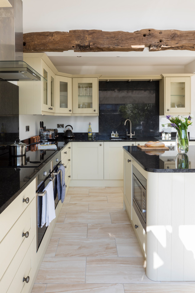 Photo of a large classic cream and black l-shaped open plan kitchen in West Midlands with a double-bowl sink, glass-front cabinets, white cabinets, granite worktops, black splashback, laminate floors, an island, black worktops and exposed beams.