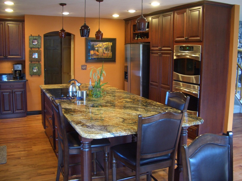 Design ideas for a large traditional u-shaped eat-in kitchen in Denver with an undermount sink, raised-panel cabinets, dark wood cabinets, granite benchtops, stainless steel appliances, light hardwood floors, with island, black splashback, stone slab splashback, beige floor and black benchtop.