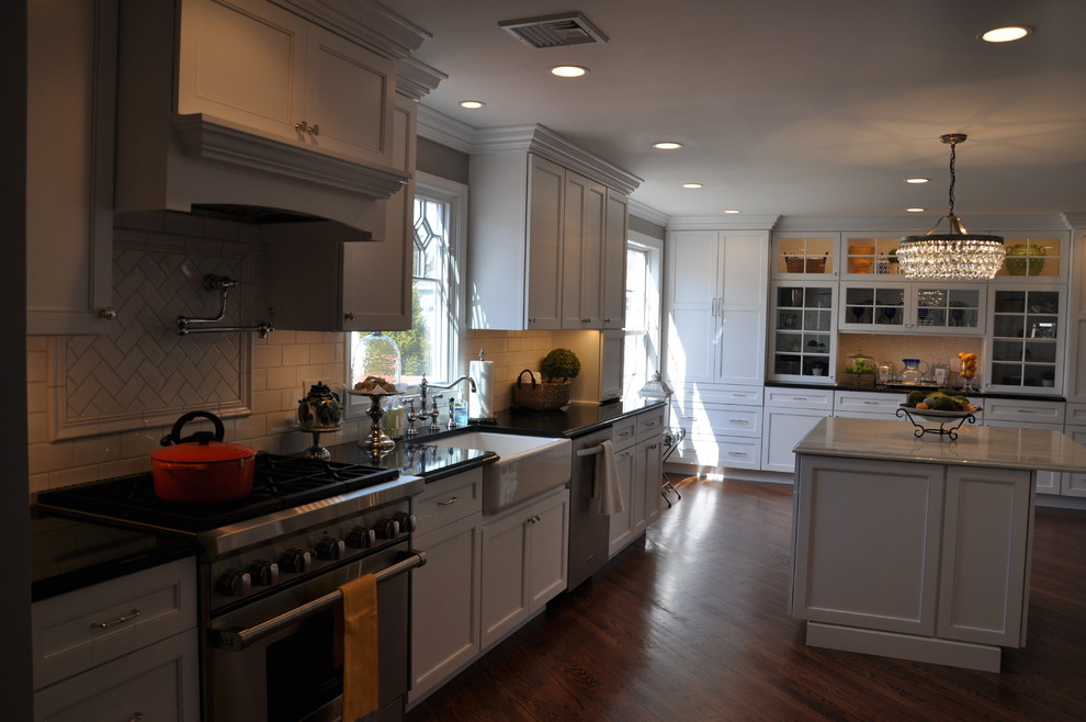 This is an example of a transitional kitchen in New York with a farmhouse sink, recessed-panel cabinets, white cabinets, quartz benchtops, white splashback, subway tile splashback, stainless steel appliances, dark hardwood floors and with island.