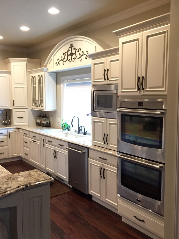 Photo of an expansive traditional u-shaped kitchen pantry in Other with an undermount sink, raised-panel cabinets, white cabinets, granite benchtops, white splashback, stainless steel appliances and multiple islands.
