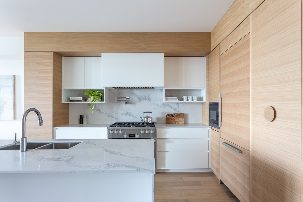 Inspiration for a modern l-shaped kitchen in Vancouver with an undermount sink, flat-panel cabinets, white cabinets, white splashback, stone slab splashback, stainless steel appliances, medium hardwood floors, with island, brown floor and white benchtop.