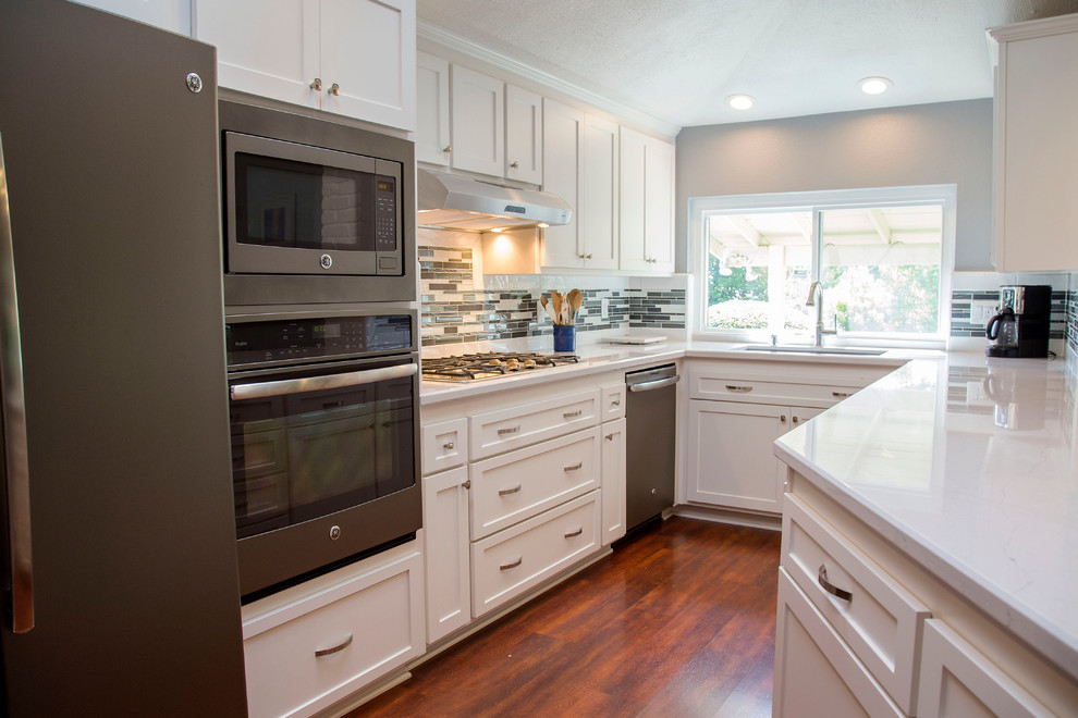 This is an example of a mid-sized transitional u-shaped eat-in kitchen in Sacramento with an undermount sink, shaker cabinets, white cabinets, quartz benchtops, multi-coloured splashback, glass tile splashback, coloured appliances, dark hardwood floors and a peninsula.