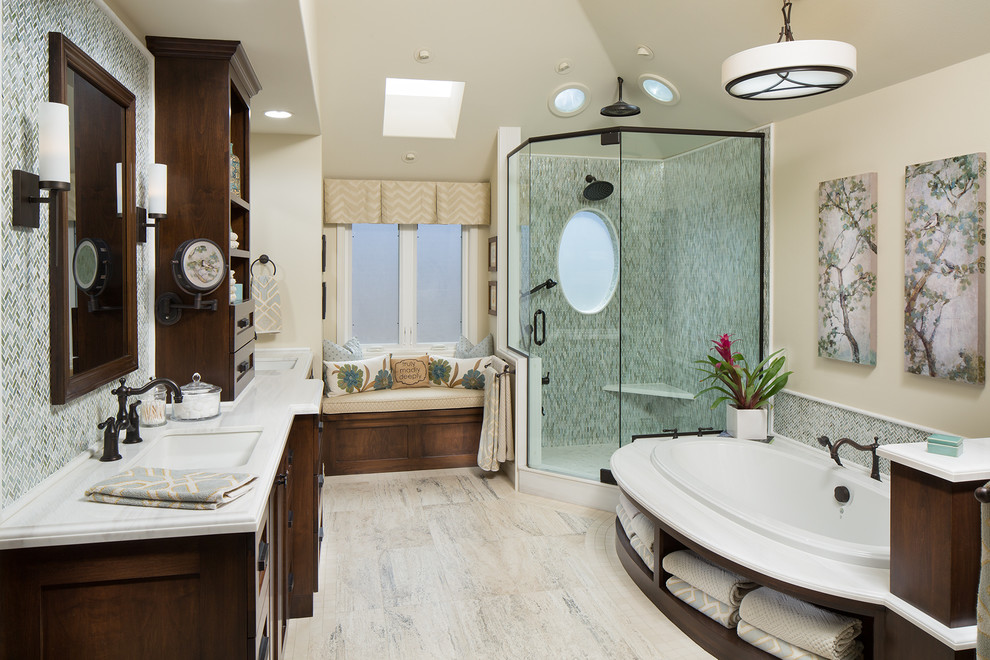 Mid-sized transitional master glass tile and multicolored tile travertine floor and beige floor drop-in bathtub photo in Orange County with shaker cabinets, dark wood cabinets, beige walls, an undermount sink, marble countertops, a one-piece toilet, a hinged shower door and white countertops