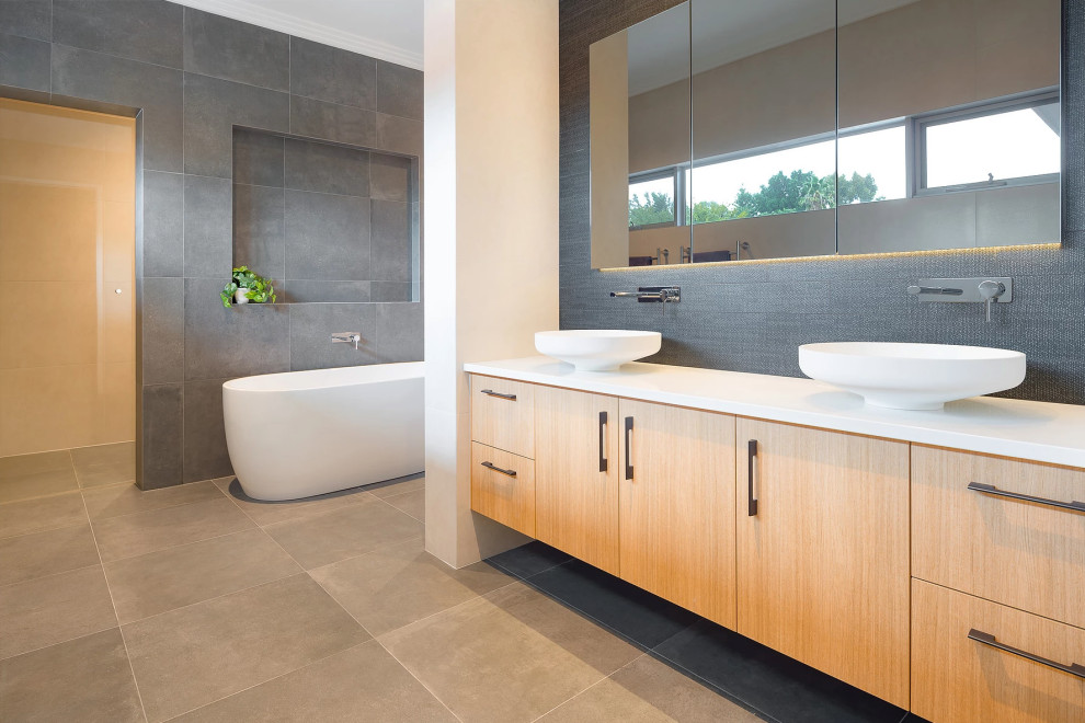 Photo of a mid-sized contemporary master bathroom in Perth with medium wood cabinets, a freestanding tub, gray tile, ceramic tile, grey walls, ceramic floors, a vessel sink, engineered quartz benchtops, grey floor and white benchtops.