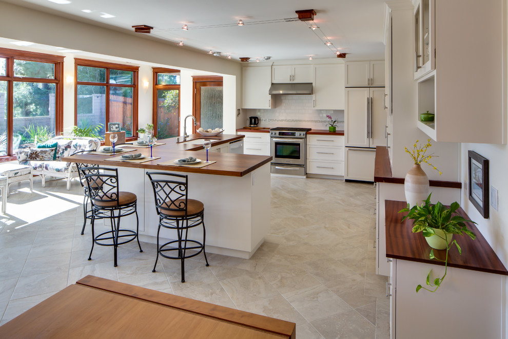 Photo of a mid-sized contemporary eat-in kitchen in San Diego with an undermount sink, shaker cabinets, white cabinets, wood benchtops, white splashback, subway tile splashback, panelled appliances, porcelain floors and with island.