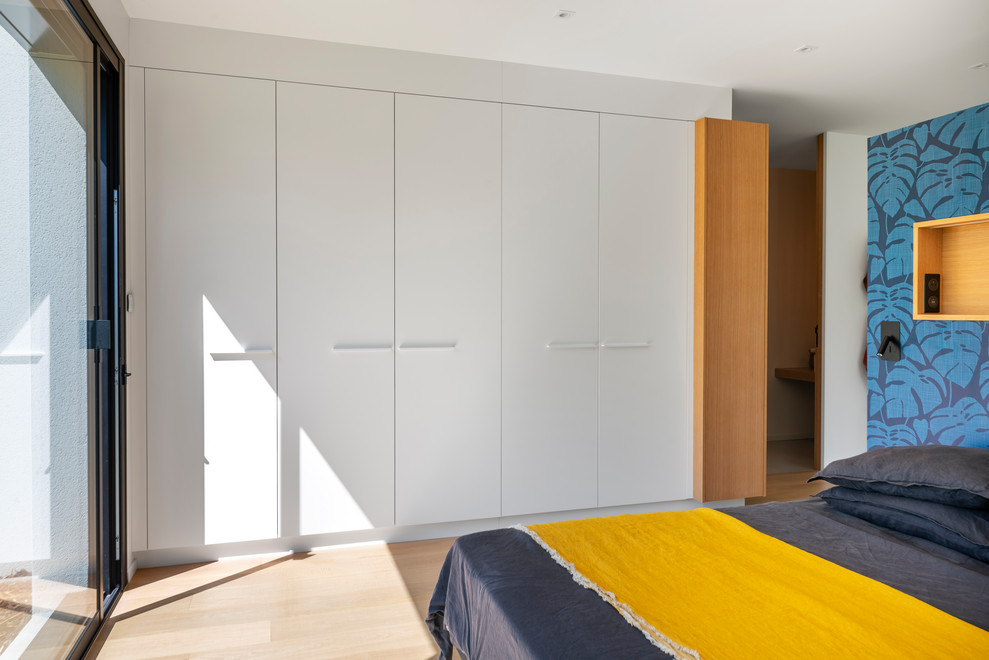 Large contemporary gender-neutral walk-in wardrobe in Nantes with beaded inset cabinets, white cabinets and light hardwood floors.