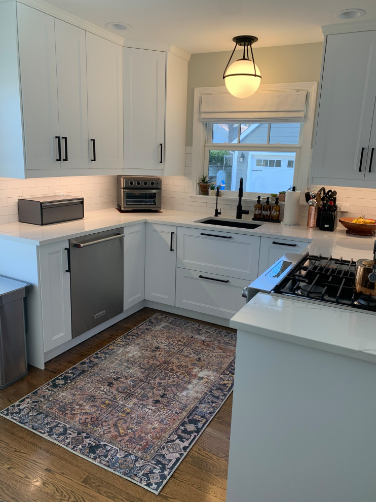 Photo of a medium sized country l-shaped kitchen/diner in Chicago with a submerged sink, shaker cabinets, white cabinets, quartz worktops, white splashback, metro tiled splashback, stainless steel appliances, medium hardwood flooring and white worktops.