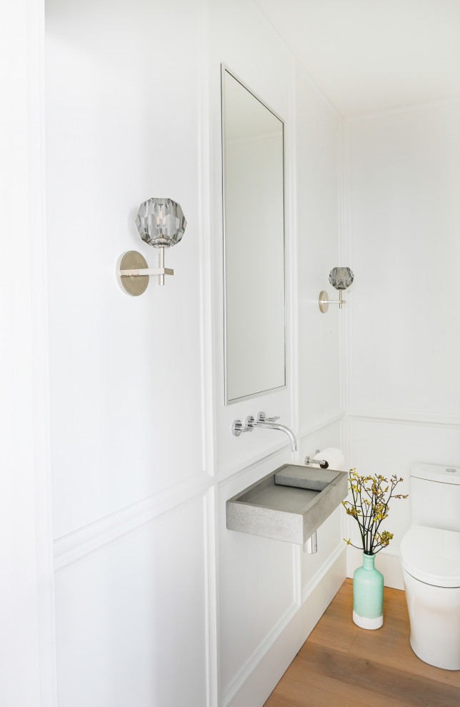 This is an example of a small traditional powder room in Vancouver with grey cabinets, a two-piece toilet, white walls, medium hardwood floors, a wall-mount sink, concrete benchtops, grey benchtops, a floating vanity and panelled walls.
