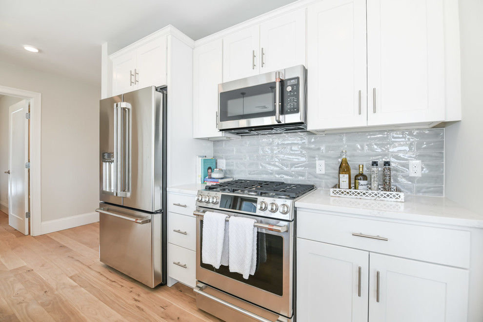 Example of a mid-sized transitional l-shaped medium tone wood floor and yellow floor eat-in kitchen design in Boston with an undermount sink, shaker cabinets, white cabinets, quartz countertops, gray backsplash, ceramic backsplash, stainless steel appliances, an island and white countertops