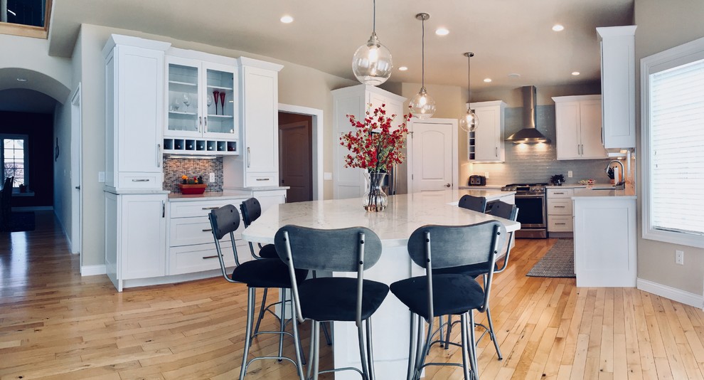 Mid-sized transitional light wood floor kitchen photo with an undermount sink, shaker cabinets, white cabinets, quartz countertops, blue backsplash, glass tile backsplash, stainless steel appliances and an island