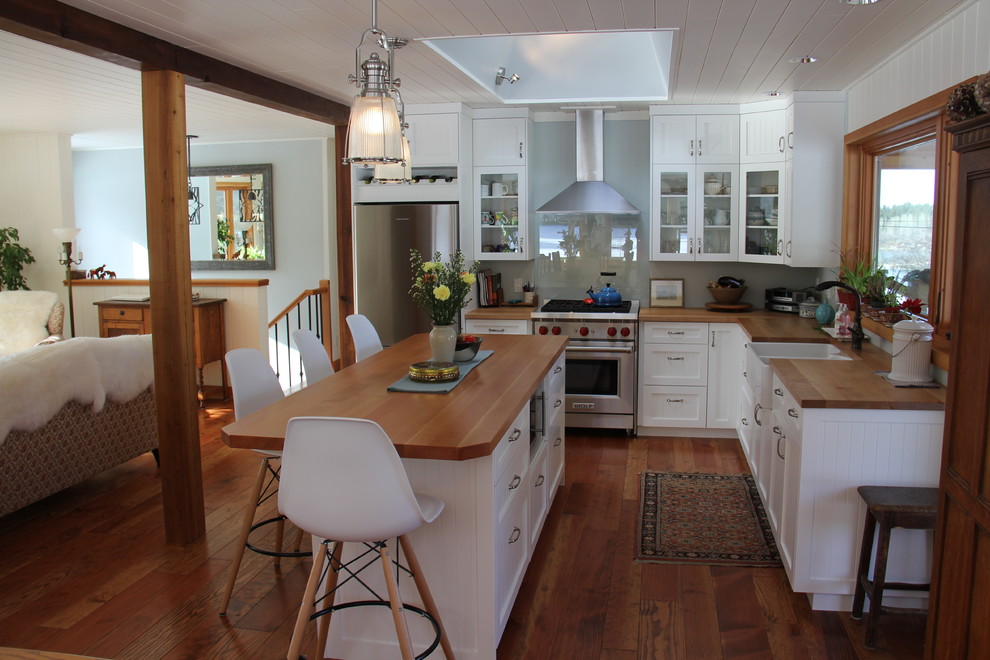 Photo of a mid-sized country l-shaped kitchen in Vancouver with a farmhouse sink, shaker cabinets, white cabinets, wood benchtops, blue splashback, glass sheet splashback, stainless steel appliances and medium hardwood floors.