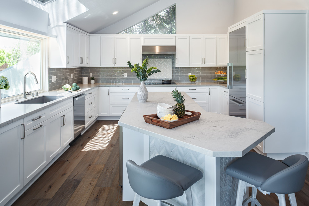 This is an example of a transitional u-shaped kitchen in San Francisco with an undermount sink, shaker cabinets, white cabinets, grey splashback, subway tile splashback, stainless steel appliances, dark hardwood floors, with island, brown floor and grey benchtop.