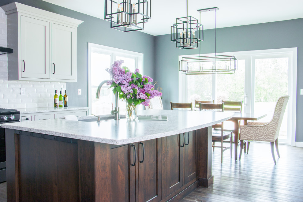 Open concept kitchen - l-shaped brown floor open concept kitchen idea with an undermount sink, flat-panel cabinets, white cabinets, white backsplash, stainless steel appliances, an island and white countertops