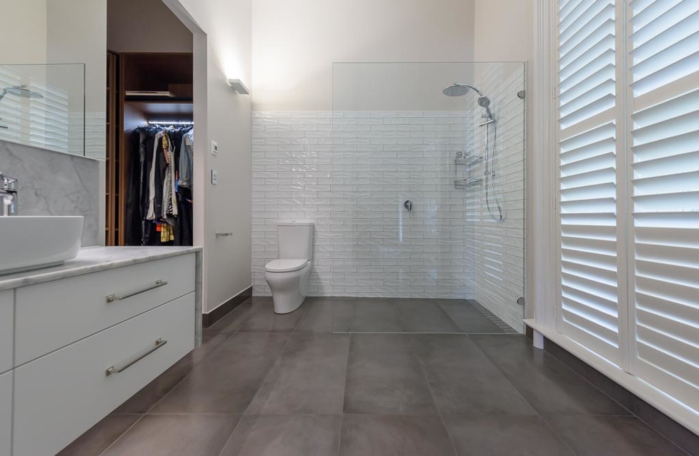 Inspiration for a mid-sized traditional bathroom in Melbourne with flat-panel cabinets, white cabinets, an open shower, a two-piece toilet, white tile, ceramic tile, white walls, porcelain floors, a vessel sink, marble benchtops, grey floor and an open shower.