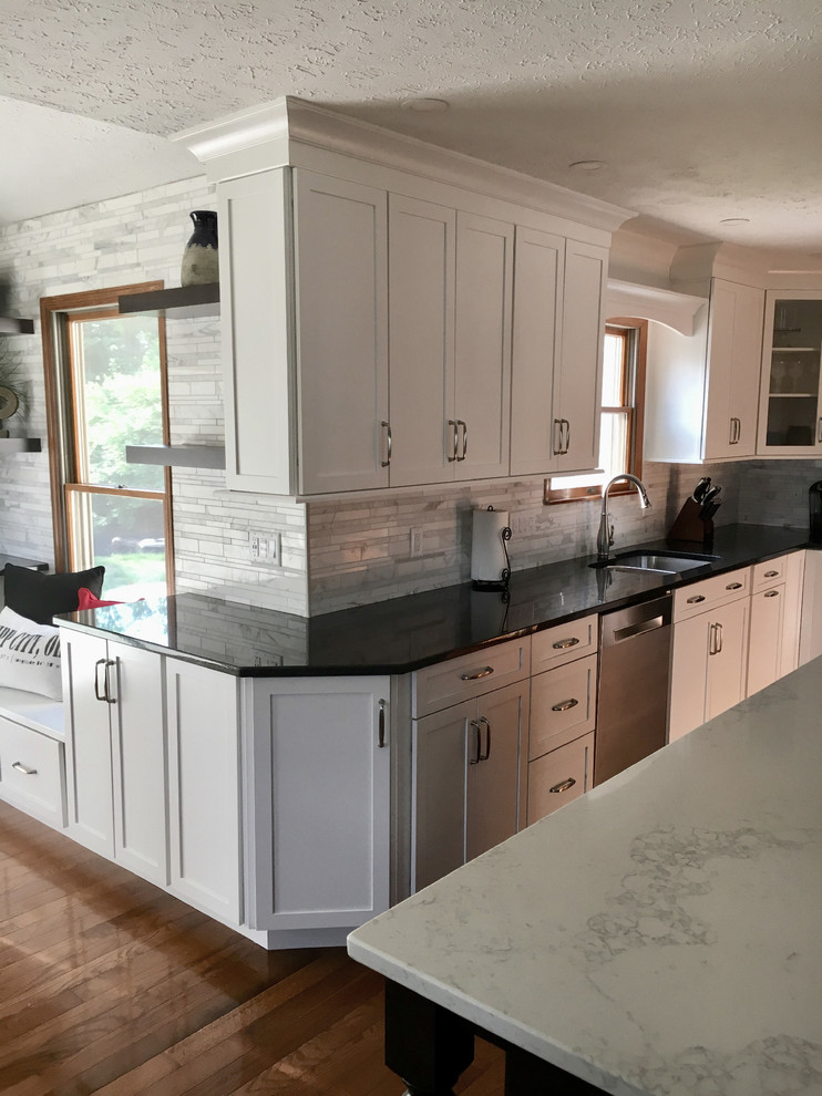 Inspiration for a large transitional single-wall medium tone wood floor eat-in kitchen remodel with an undermount sink, shaker cabinets, white cabinets, granite countertops, multicolored backsplash, marble backsplash, stainless steel appliances, an island and black countertops