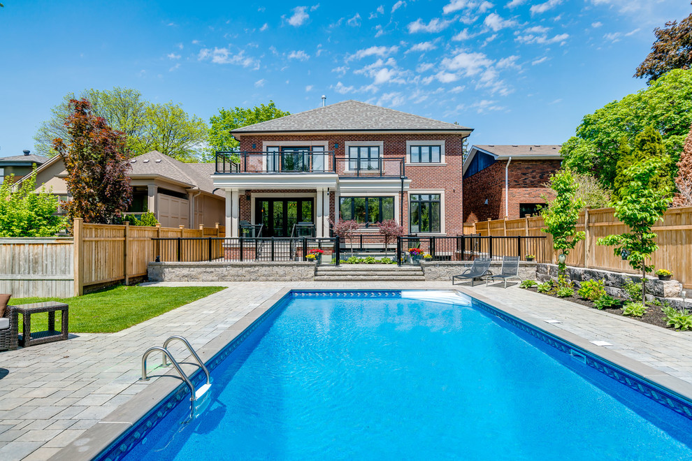 Large transitional backyard rectangular lap pool in Toronto with a pool house and natural stone pavers.