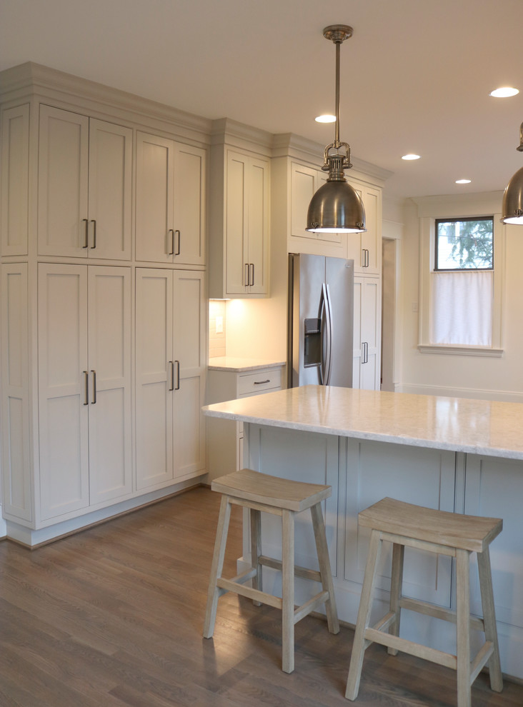 Large transitional galley medium tone wood floor and brown floor enclosed kitchen photo with a farmhouse sink, shaker cabinets, gray cabinets, quartzite countertops, stainless steel appliances, beige backsplash, subway tile backsplash and a peninsula