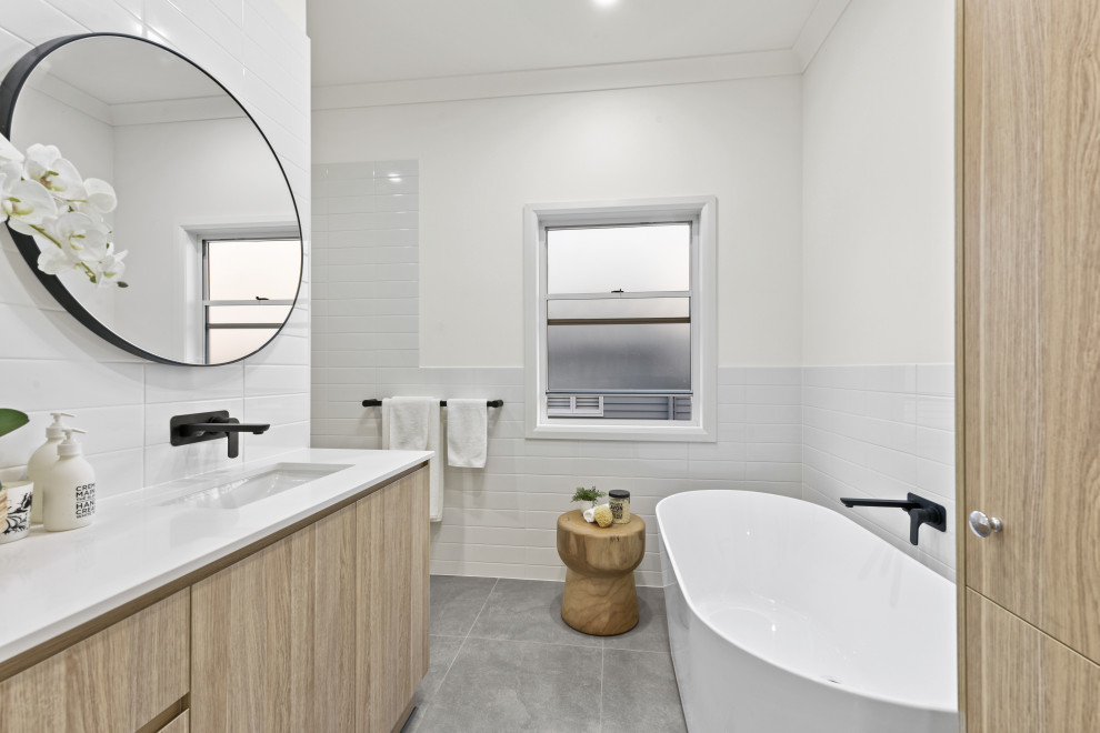 This is an example of a mid-sized contemporary kids bathroom in Brisbane with a freestanding tub, white tile, subway tile, white walls, porcelain floors, an undermount sink, engineered quartz benchtops, a hinged shower door, white benchtops, flat-panel cabinets, light wood cabinets and grey floor.