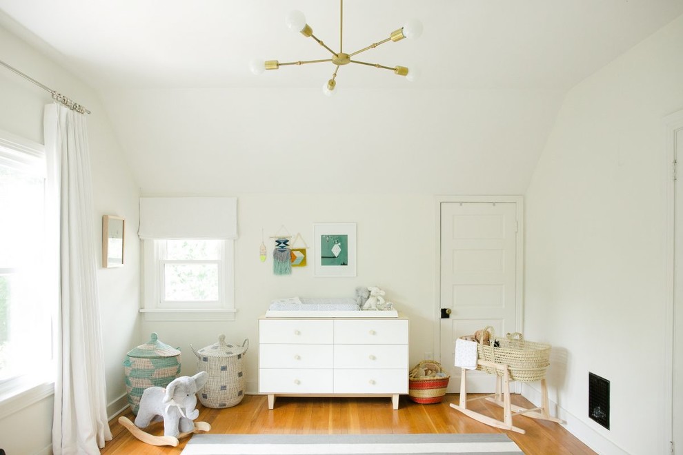 This is an example of a mid-sized eclectic gender-neutral nursery in Nashville with white walls, medium hardwood floors and brown floor.
