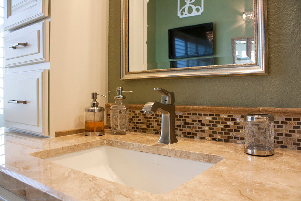 Example of a large transitional master multicolored tile and mosaic tile travertine floor drop-in bathtub design with raised-panel cabinets, white cabinets, a one-piece toilet, green walls, an undermount sink and marble countertops