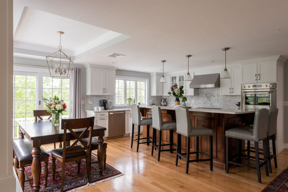Inspiration for a large transitional l-shaped medium tone wood floor, brown floor and coffered ceiling eat-in kitchen remodel in Boston with an undermount sink, shaker cabinets, white cabinets, quartz countertops, gray backsplash, subway tile backsplash, stainless steel appliances, an island and white countertops