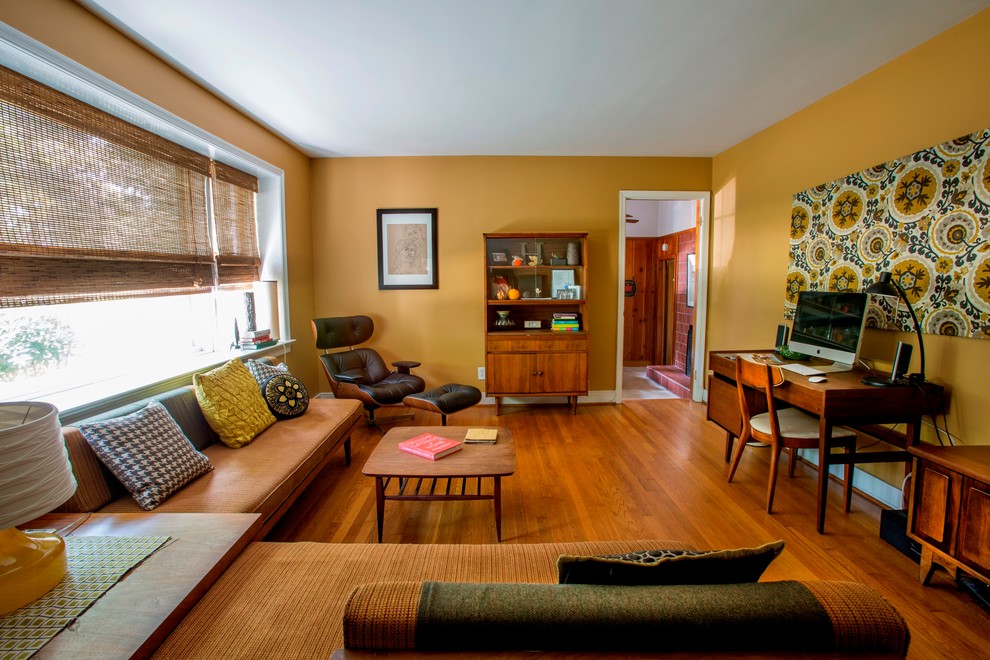 This is an example of a large midcentury study room in Richmond with light hardwood floors, no fireplace, a freestanding desk, brown floor and orange walls.