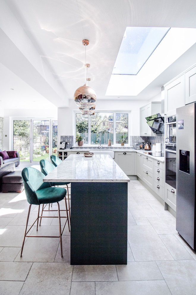 Inspiration for a mid-sized transitional l-shaped open plan kitchen in London with a farmhouse sink, shaker cabinets, granite benchtops, blue splashback, ceramic splashback, stainless steel appliances, limestone floors, with island, grey floor and white benchtop.