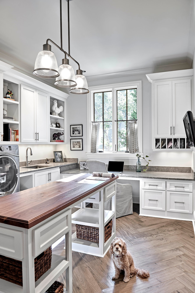 Inspiration for a mid-sized transitional utility room in Nashville with an undermount sink, white cabinets, white walls, light hardwood floors, open cabinets, limestone benchtops, a side-by-side washer and dryer, brown floor and brown benchtop.