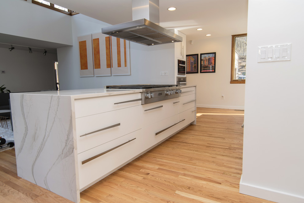 This is an example of a large modern galley eat-in kitchen in Baltimore with an undermount sink, flat-panel cabinets, white cabinets, quartz benchtops, stainless steel appliances, medium hardwood floors, with island and white benchtop.