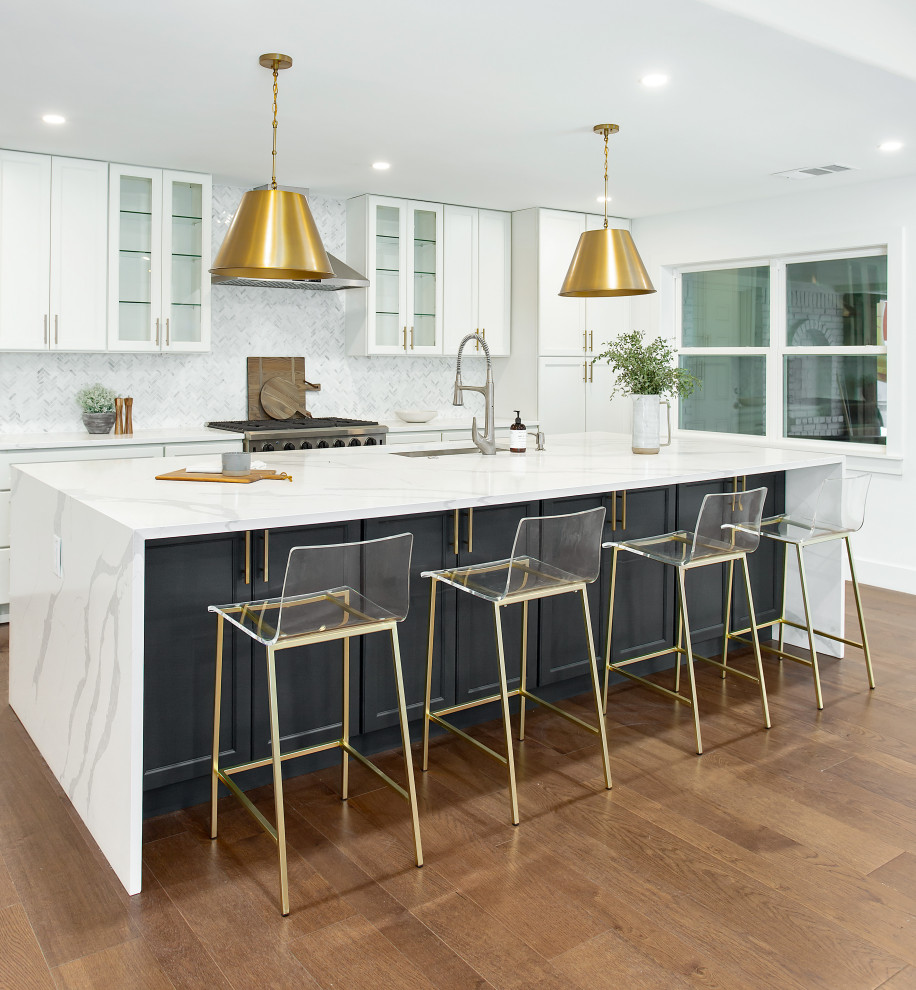 This is an example of a large contemporary galley open plan kitchen in Dallas with an undermount sink, shaker cabinets, white cabinets, quartz benchtops, white splashback, marble splashback, stainless steel appliances, medium hardwood floors, with island, brown floor and white benchtop.