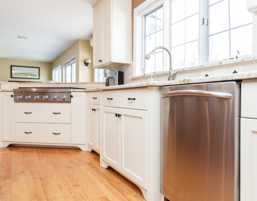 Mid-sized transitional u-shaped light wood floor enclosed kitchen photo in Boston with a double-bowl sink, recessed-panel cabinets, white cabinets, granite countertops, beige backsplash, stone tile backsplash, stainless steel appliances and an island