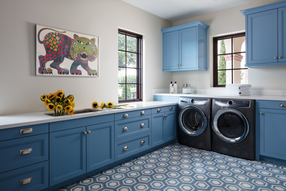 Immagine di una sala lavanderia tradizionale con lavello sottopiano, ante con riquadro incassato, ante blu, top in quarzo composito, pareti bianche, lavatrice e asciugatrice affiancate, pavimento multicolore e top bianco