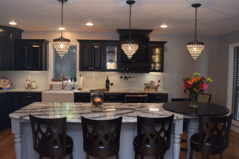 Transitional medium tone wood floor kitchen photo in Chicago with a farmhouse sink, raised-panel cabinets, black cabinets, quartz countertops, white backsplash, glass tile backsplash, stainless steel appliances and an island