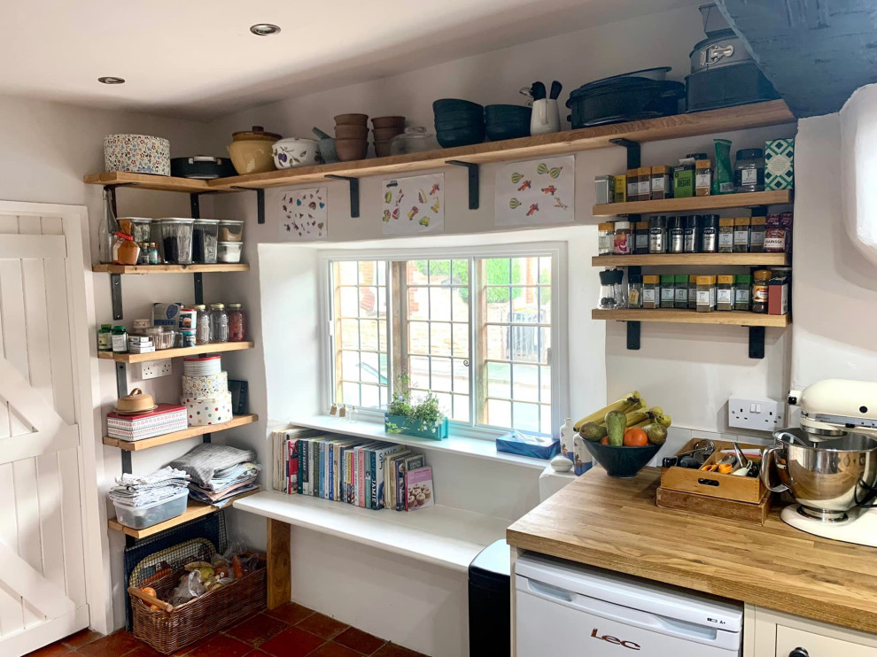 Small traditional u-shaped enclosed kitchen in Other with a double-bowl sink, shaker cabinets, white cabinets, wood worktops, white splashback, ceramic splashback, white appliances, terracotta flooring, no island, red floors, brown worktops and exposed beams.