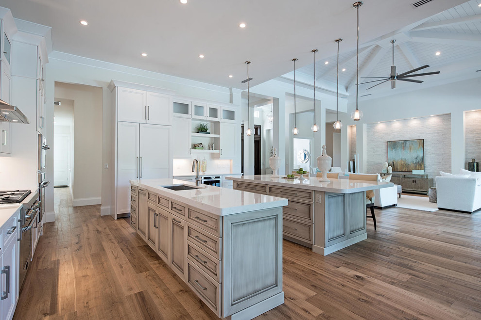 Design ideas for a transitional open plan kitchen in Miami with an undermount sink, recessed-panel cabinets, white splashback, stainless steel appliances, medium hardwood floors and multiple islands.