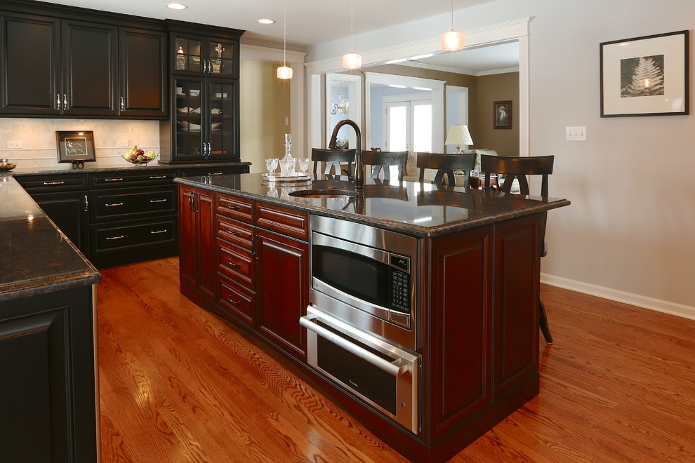 Large traditional u-shaped kitchen in Chicago with a drop-in sink, raised-panel cabinets, black cabinets, beige splashback, stainless steel appliances, medium hardwood floors and with island.