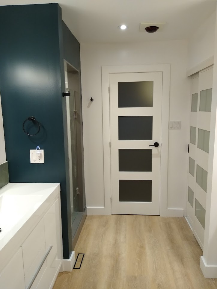 This is an example of a mid-sized modern master bathroom in Toronto with flat-panel cabinets, white cabinets, a freestanding tub, a corner shower, a one-piece toilet, brown tile, porcelain tile, white walls, vinyl floors, an integrated sink, onyx benchtops, beige floor, a hinged shower door, white benchtops, a single vanity, a freestanding vanity and planked wall panelling.