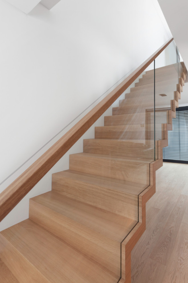 This is an example of a contemporary wood floating staircase in Berlin with wood risers and glass railing.