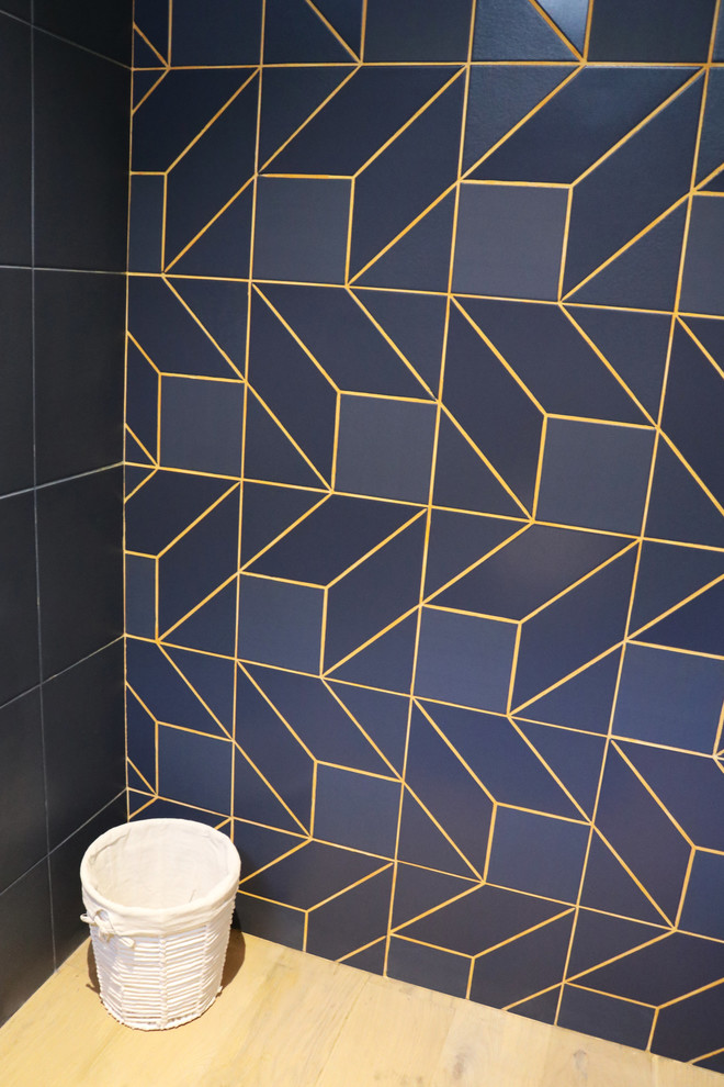 Inspiration for a mid-sized contemporary powder room in Bordeaux with a wall-mount toilet, blue tile, ceramic tile, orange walls, light hardwood floors, tile benchtops, brown floor and blue benchtops.