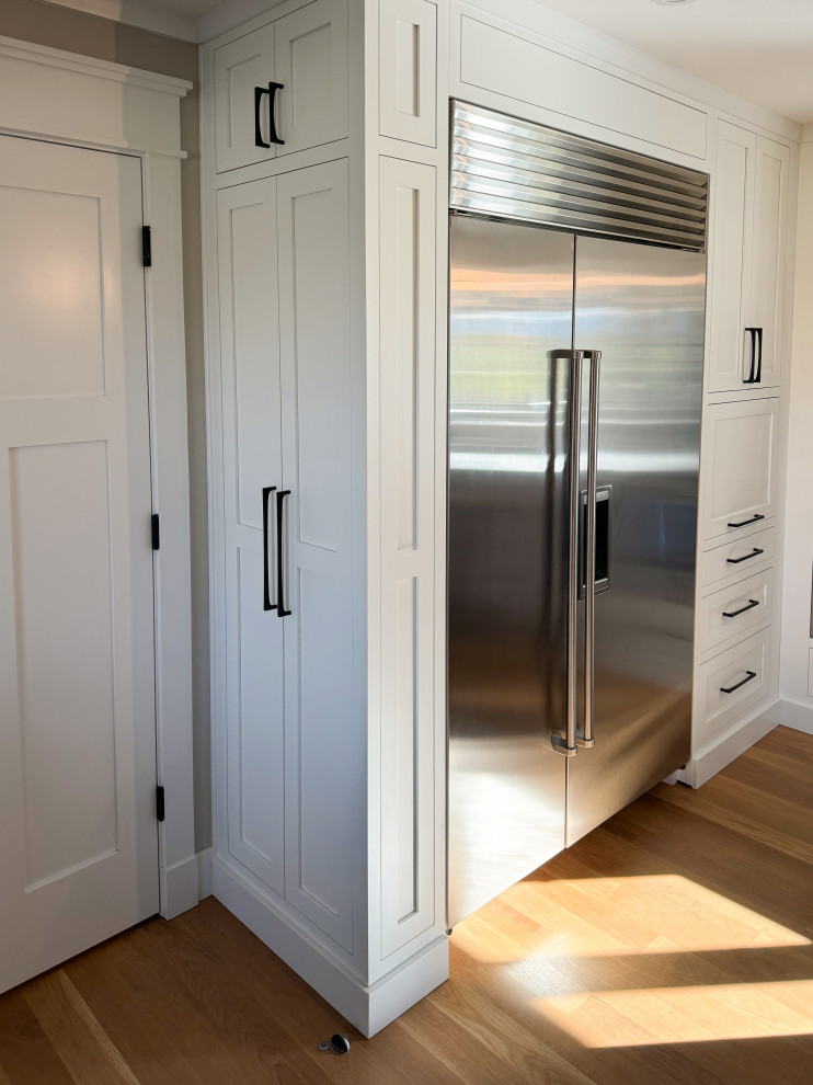 Inspiration for a mid-sized transitional l-shaped medium tone wood floor and brown floor eat-in kitchen remodel with an undermount sink, shaker cabinets, white cabinets, white backsplash, stainless steel appliances, an island and white countertops