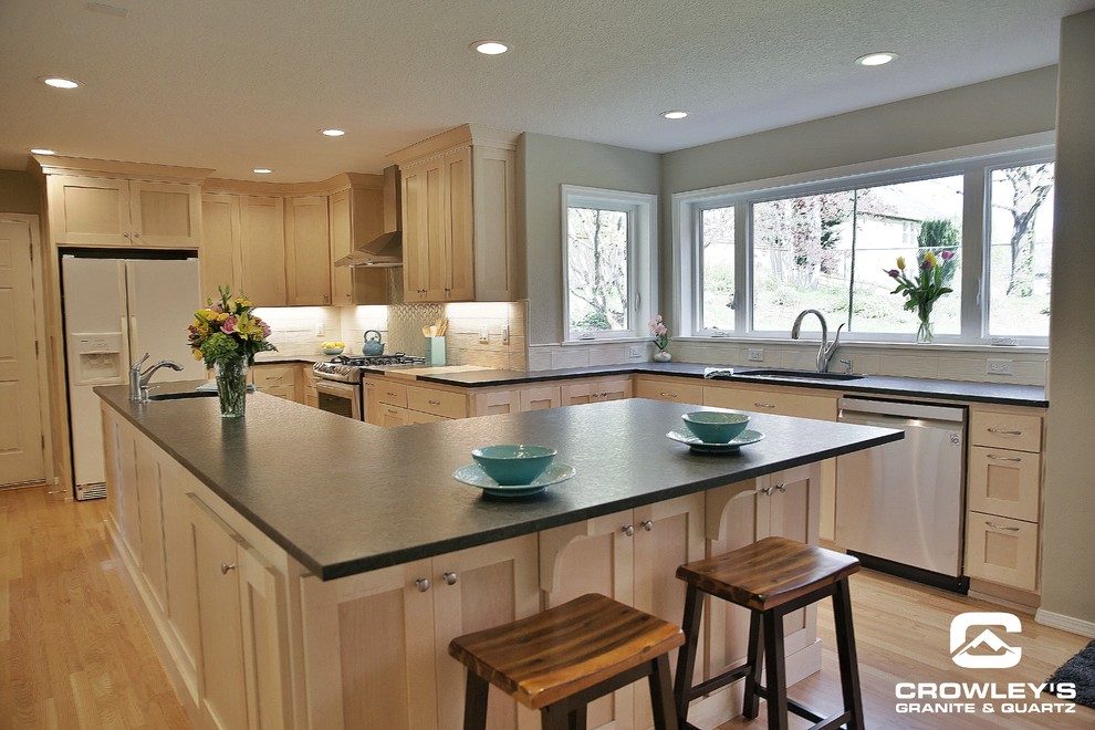This is an example of an expansive contemporary l-shaped eat-in kitchen in Portland with an undermount sink, shaker cabinets, light wood cabinets, granite benchtops, stainless steel appliances, light hardwood floors, with island, beige floor and black benchtop.
