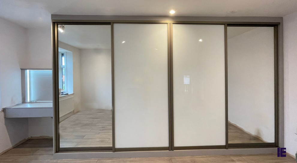 Photo of a small modern built-in wardrobe in London with white cabinets, plywood flooring, brown floors, a wood ceiling and feature lighting.