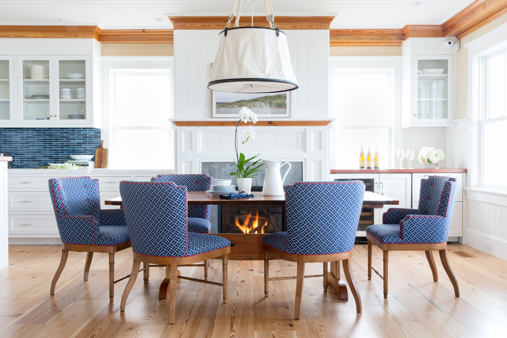 Mid-sized beach style separate dining room in Boston with white walls, light hardwood floors, a standard fireplace, a stone fireplace surround and beige floor.