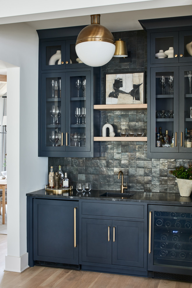 Photo of a traditional single-wall wet bar in Atlanta with a submerged sink, glass-front cabinets, black cabinets, granite worktops, black splashback, light hardwood flooring and black worktops.
